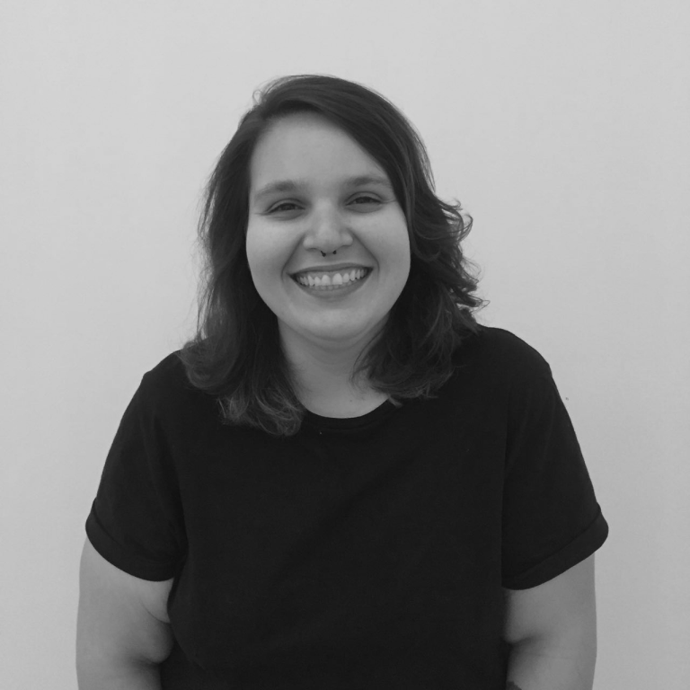 Picture of a white woman smiling with brown hair on their shoulders, black t-shirt